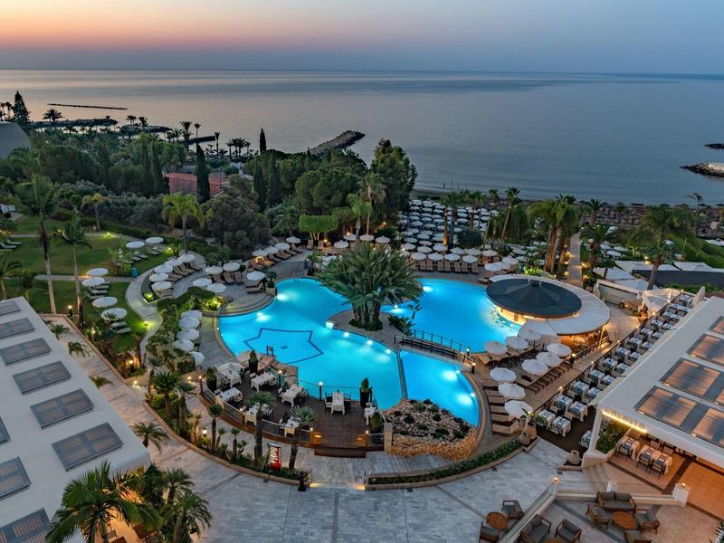 Aerial view of a lit hotel pool at sunset overlooking the sea.