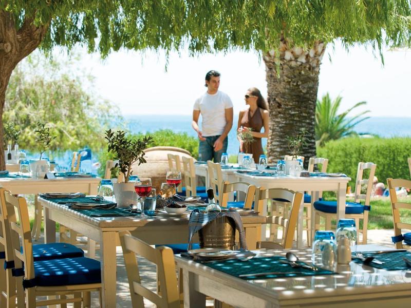 Outdoor restaurant with set tables and couple in the background with sea view.