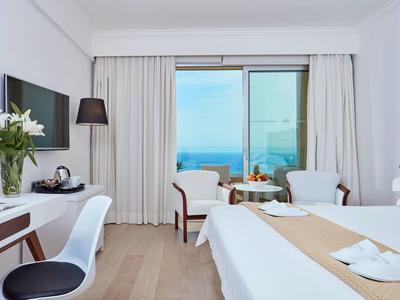 Helles Hotelzimmer mit Meerblick, weißen Möbeln und einem gemütlichen Sitzbereich am Fenster.