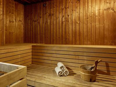 Warmer Wellnessbereich mit Holzwänden, Bänken, Handtüchern und einem Holzeimer mit Schöpfkelle.