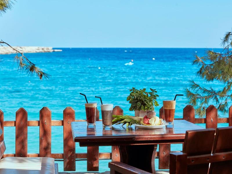 Tisch mit Getränken und Snacks vor Blick auf das blaue Meer und einen klaren Himmel.