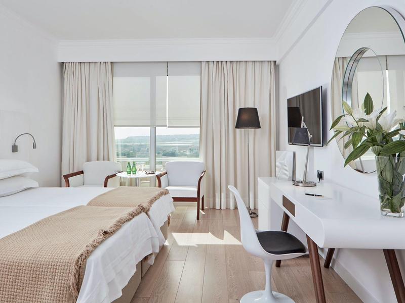 Modernes Hotelzimmer mit Doppelbett, Schreibtisch, Fernseher und großem Fenster mit Blick nach draußen.