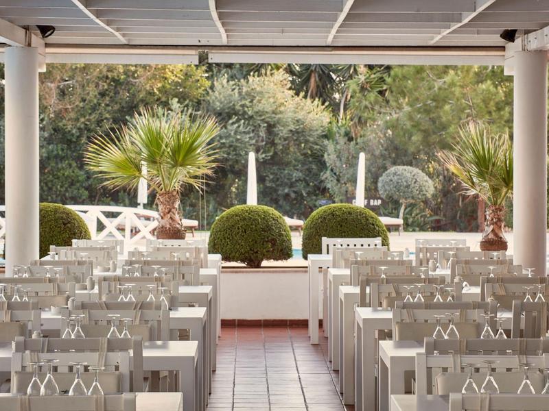 Außenbereich mit weißen Stühlen und dekorativen Pflanzen in einem Hotel oder Veranstaltungsort.