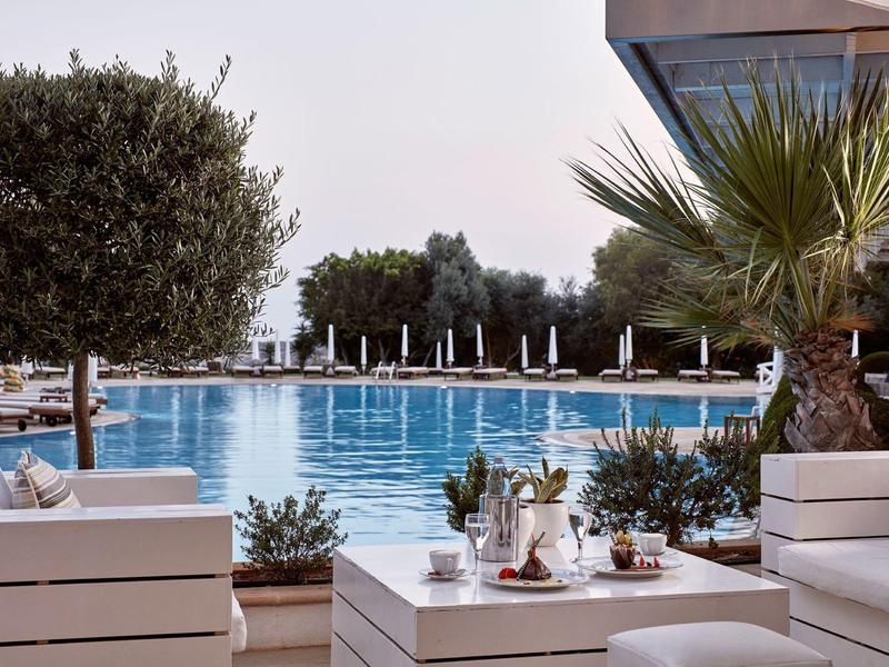 Moderner Außenbereich mit weißer Lounge und Blick auf einen Pool mit Palmen und Sonnenschirmen.