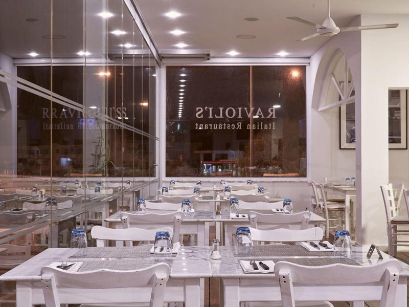 Modernes Restaurant mit weißen Tischen und Stühlen, gedeckt mit Tellern und Gläsern bei Nacht