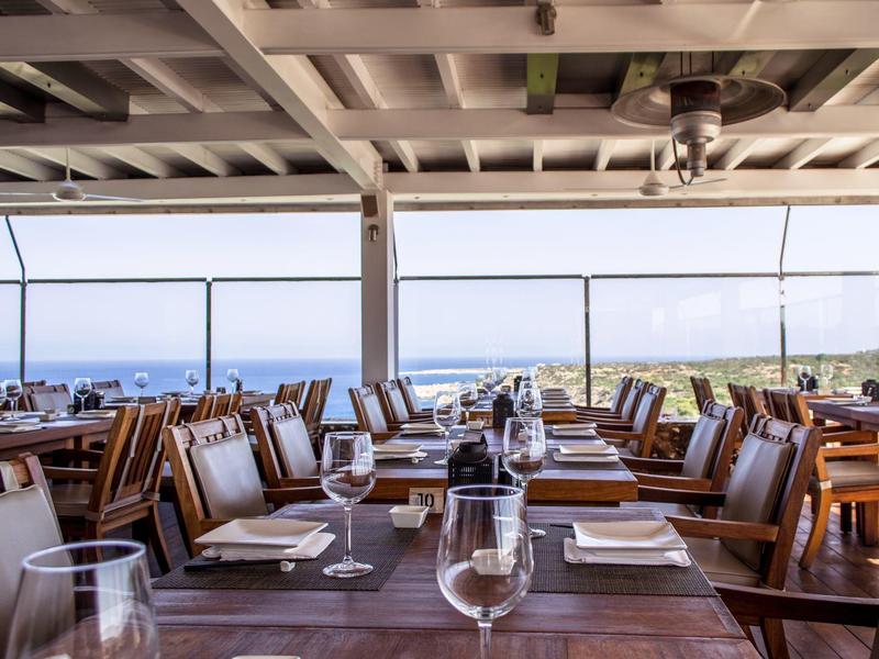 Restaurantterrasse mit Holztischen und Stühlen mit Blick auf das Meer bei klarem Himmel