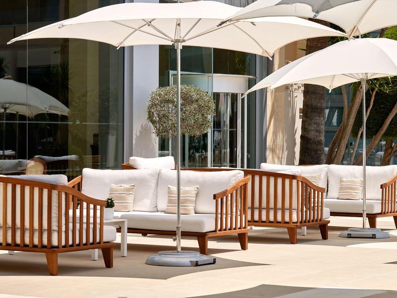 Loungebereich mit Holzmöbeln und großen weißen Sonnenschirmen im Außenbereich eines Hotels.