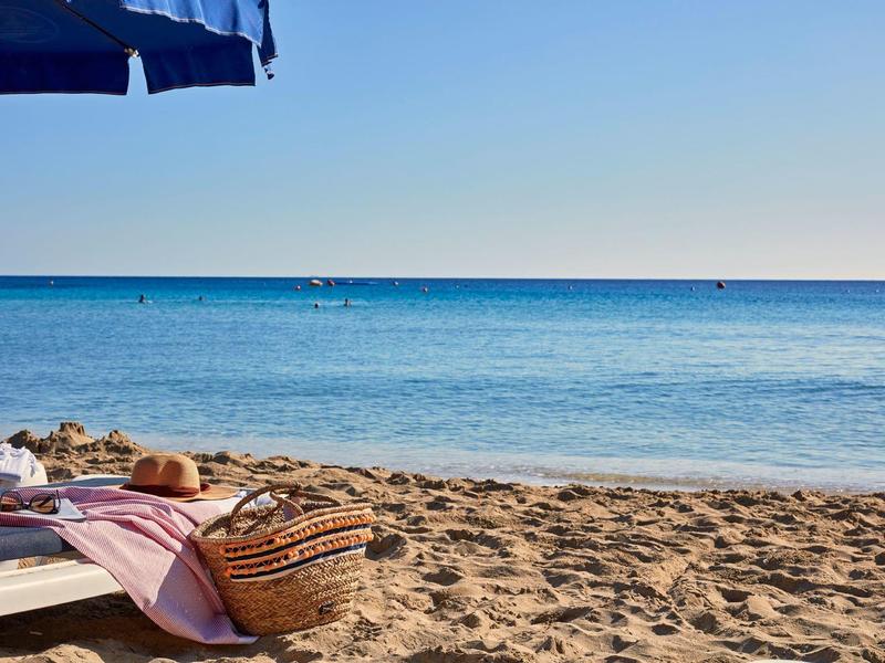 Strand mit Liegestuhl, Sonnenschirm und Blick auf das ruhige blaue Meer bei klarem Himmel.