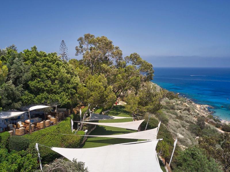 Blick auf eine Küste mit Bäumen, Sonnensegeln und Meer im Hintergrund.