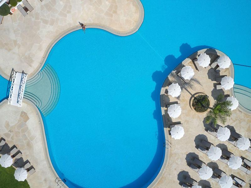 Großer Pool mit weiß-schattierten Sonnenschirmen und Liegestühlen neben einer Terrasse.