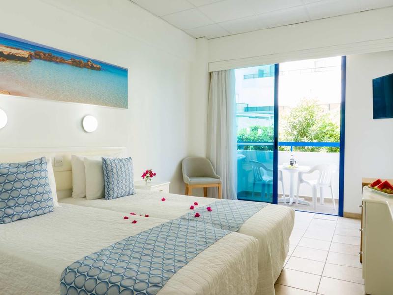 Helles Schlafzimmer mit zwei Einzelbetten, Balkon mit Glasgeländer und weißen Wänden.