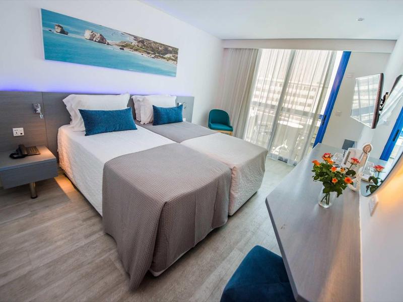 Modernes Hotelzimmer mit zwei Betten, grauen Decken, blauen Akzenten und Balkon mit Meerblick.