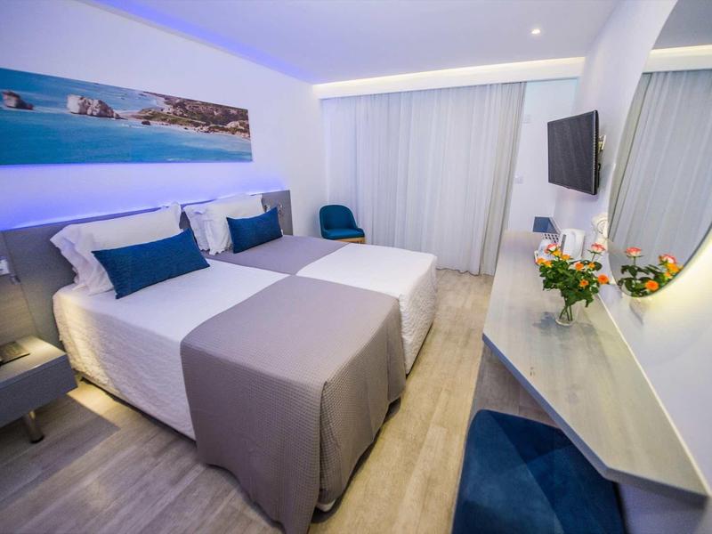 Modernes Hotelzimmer mit zwei Betten, blauer Beleuchtung, großem Spiegel und Schreibtisch.