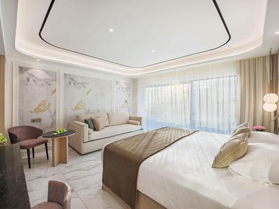 Chambre d'hôtel moderne avec grand lit, canapé et art mural discret dans un cadre lumineux.