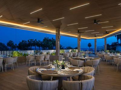 Espace de restauration ouvert avec tables dressées et toit éclairé au crépuscule.