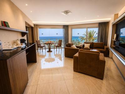 Chambre d'hôtel avec vue sur la mer, canapé, TV et table à manger avec chaises.