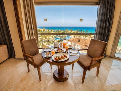 Coin repas avec table pour deux dressée pour le petit-déjeuner, vue sur la mer et la ville.