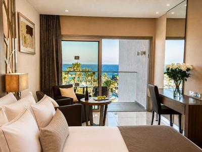 Chambre d'hôtel lumineuse avec lit, coin salon et balcon avec vue sur la mer.