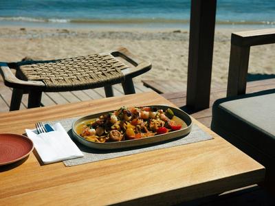 Une table en bois avec de la nourriture et une plage en arrière-plan sous un parasol.