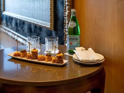 Une table en bois avec une bouteille d'eau minérale, deux verres et une assiette de petites bouchées.