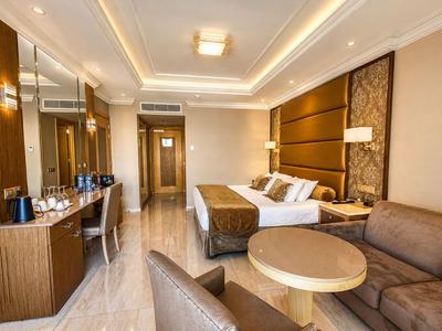 Chambre d'hôtel moderne avec lit, coin salon et bureau dans des tons chauds.