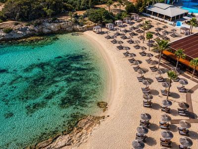 Plage de sable avec parasols ombragés à côté d'eau turquoise claire et un restaurant.