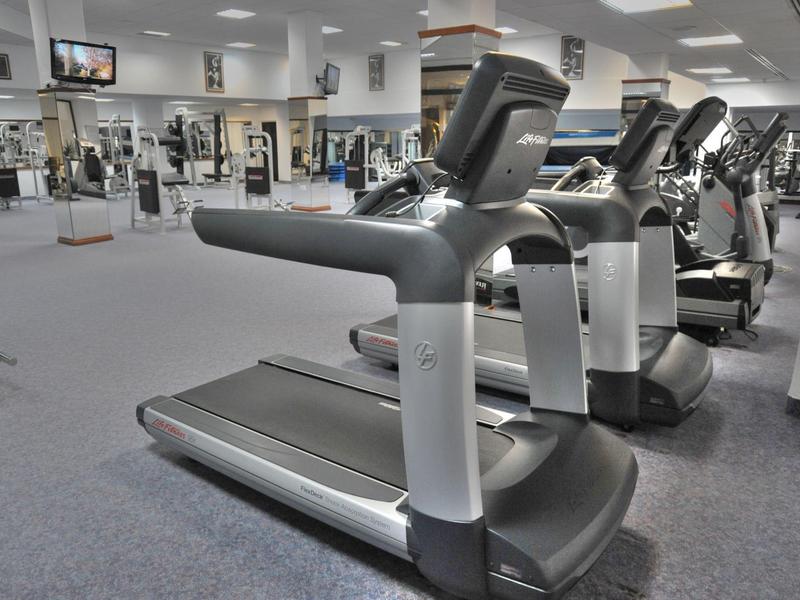 Moderne Laufbänder in einem hellen Fitnessstudio mit grauem Teppichboden.