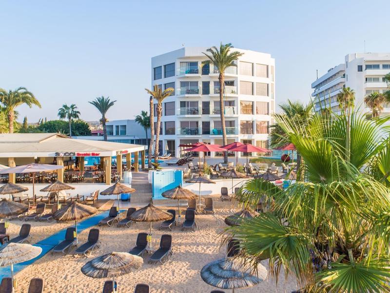 Strandhotel mit Liegestühlen, Sonnenschirmen und Palmen am Sandstrand bei klarem Wetter.