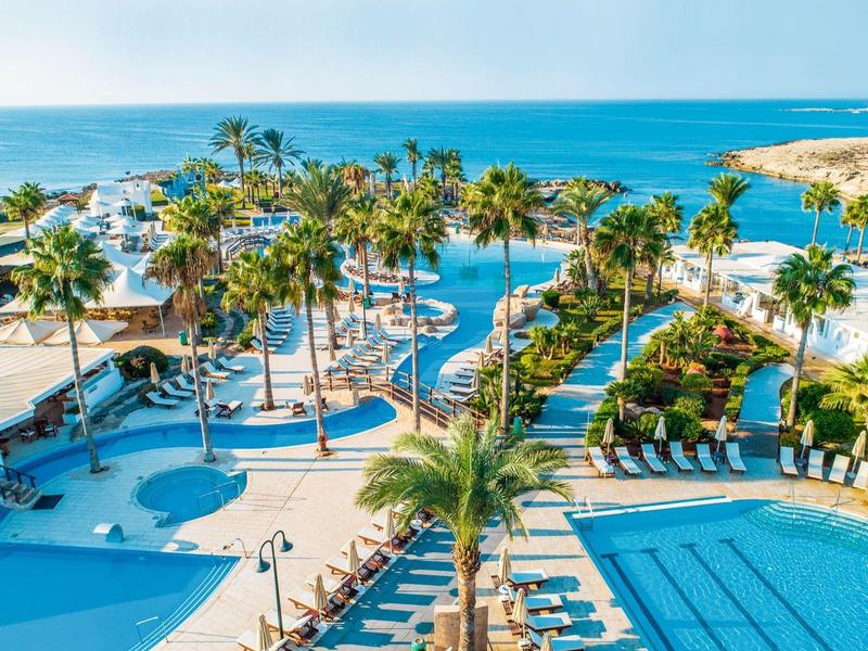 Luxuriöser Hotelpool mit Palmen und Blick auf das Meer bei sonnigem Wetter.