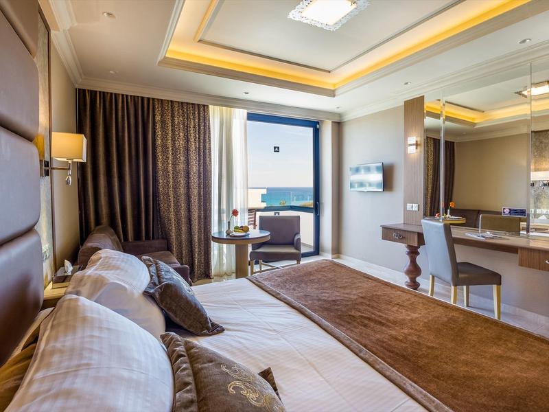 Modernes Hotelzimmer mit großem Bett, Sitzbereich und Meerblick durch das Fenster.