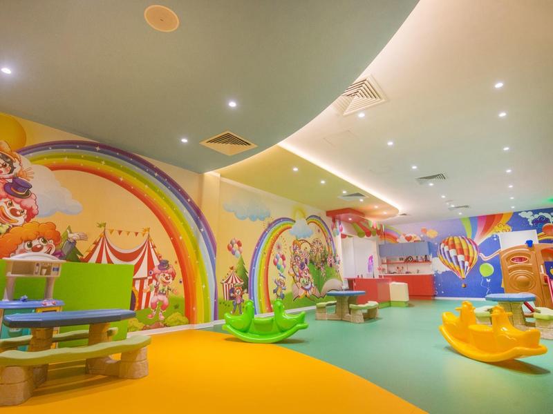 Bunter Indoor-Spielbereich mit Wandgemälden, Spielgeräten und weichem Boden für Kinder.