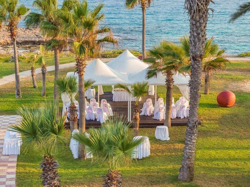 Grüne Gartenfläche mit Pavillon, Stühlen und Blick auf das Meer in einem Ferienresort.