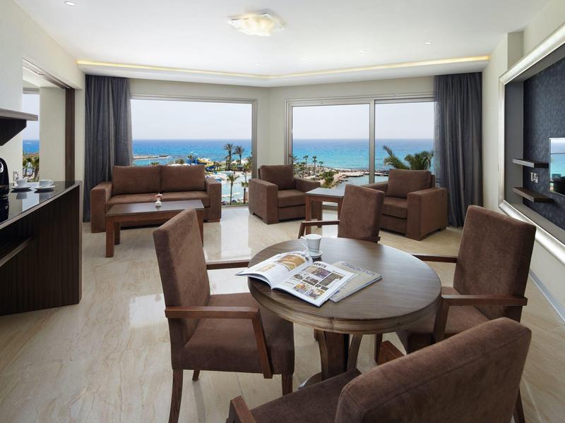 Helles Hotelzimmer mit Sitzgruppe und Meerblick durch große Fenster.