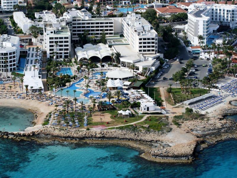 Hotelanlage mit Pools und Strand an einer felsigen Küste neben klarem blauem Wasser.