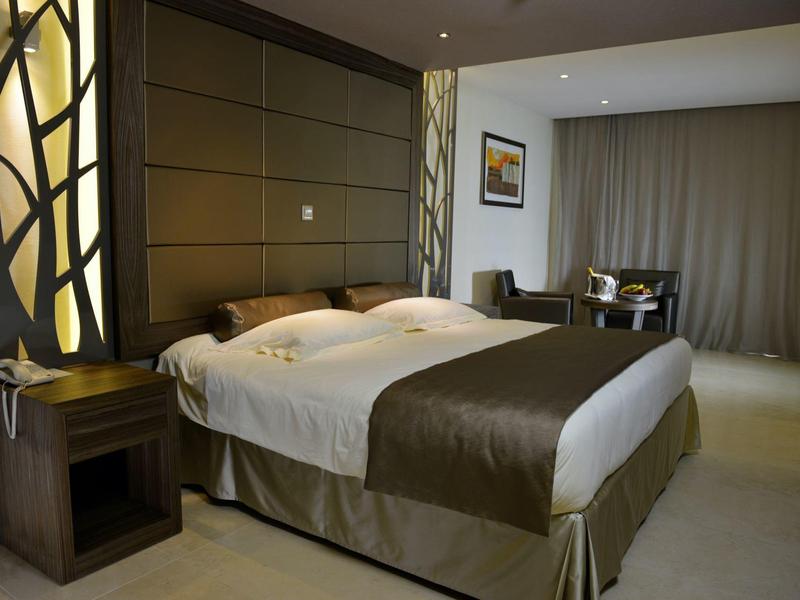 Helles Hotelzimmer mit großem Doppelbett, elegantem Nachttisch und Sitzbereich am Fenster.