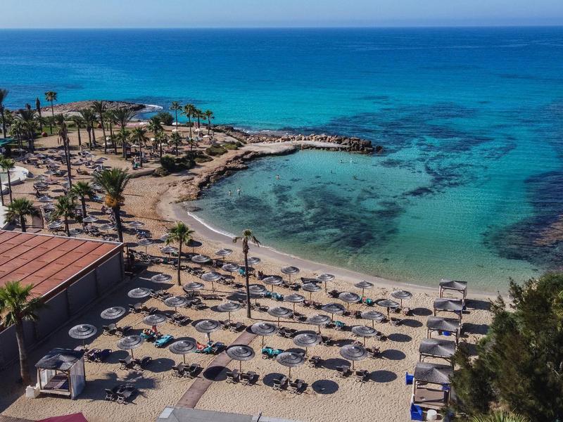 Überblick über einen Hotelstrand mit Sonnenliegen, Pool und klarem blauem Meer.