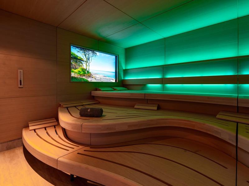 Moderne Sauna mit geschwungenen Holzbänken und grüner LED-Beleuchtung.