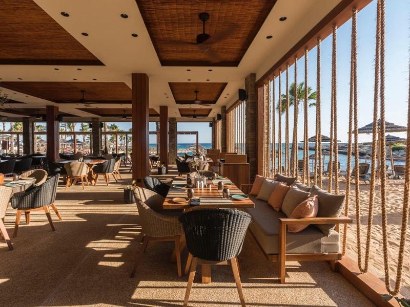 Gemütlicher Außenbereich eines Strandrestaurants mit Holzmöbeln und Blick auf das Meer.