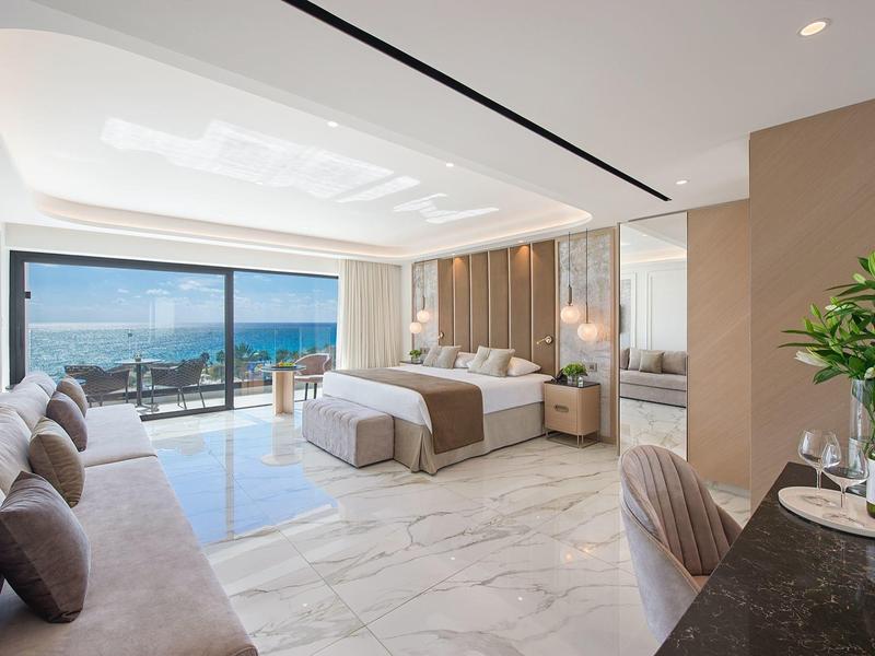 Modernes Hotelzimmer mit Meerblick, Doppelbett, Sofa und Balkon bei Tageslicht.