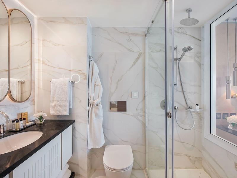 Modernes Hotelbadezimmer mit Dusche, Toilette, Waschtisch und Marmorfliesen.