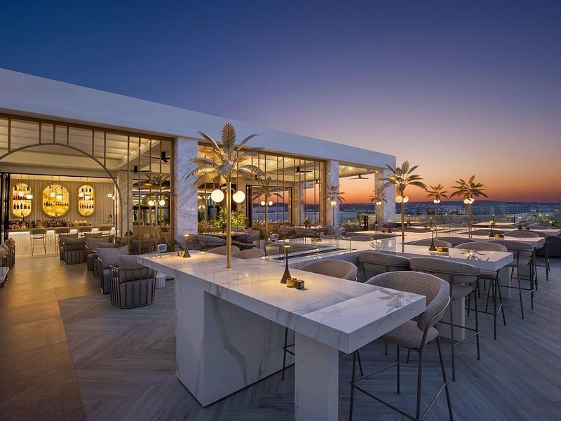 Moderner Außenbereich einer Hotelbar mit Sitzgelegenheiten und Meerblick bei Sonnenuntergang.