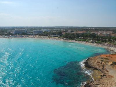 Türkisfarbenes Meer trifft auf goldenen Sandstrand und felsige Küste unter blauem Himmel.