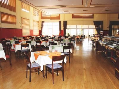 Großer, heller Speisesaal mit Holzboden, vielen Tischen und Stühlen und Buffetbereich rechts.