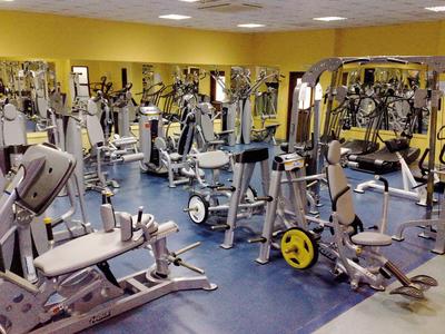 Großer Fitnessraum mit zahlreichen Trainingsgeräten auf blauem Boden und gelben Wänden.