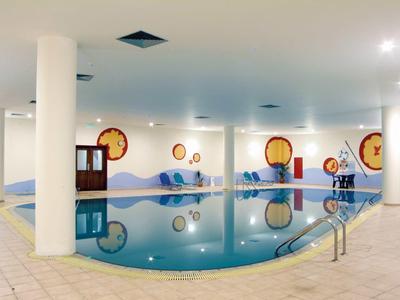 Innenpool mit rundem Becken, weißen Säulen, Wanddekorationen und heller Fliesenfläche.