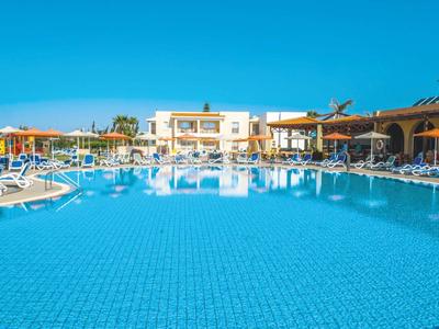 Gran piscina de hotel con tumbonas y cielo azul despejado de fondo.