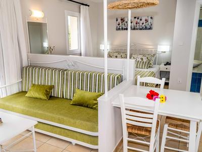 Helles Wohnzimmer mit grün gestreiftem Sofa, weißem Esstisch und Stühlen, hellem Fliesenboden und Wanddeko.