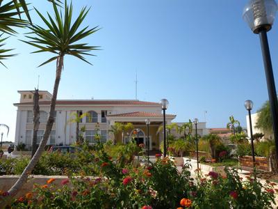 Edificio del hotel con jardín, palmeras y farolas bajo un cielo azul claro.