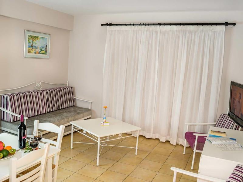 Helles Wohnzimmer mit gestreiftem Sofa, weißem Tisch, Stühlen und TV an weißer Wand.