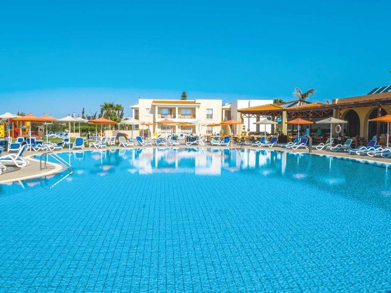 Großer Außenpool mit Liegestühlen und Sonnenschirmen bei klarem Himmel in einem Hotelresort.